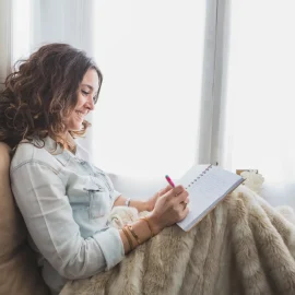 Femeie care scrie într-un jurnal într-un fotoliu